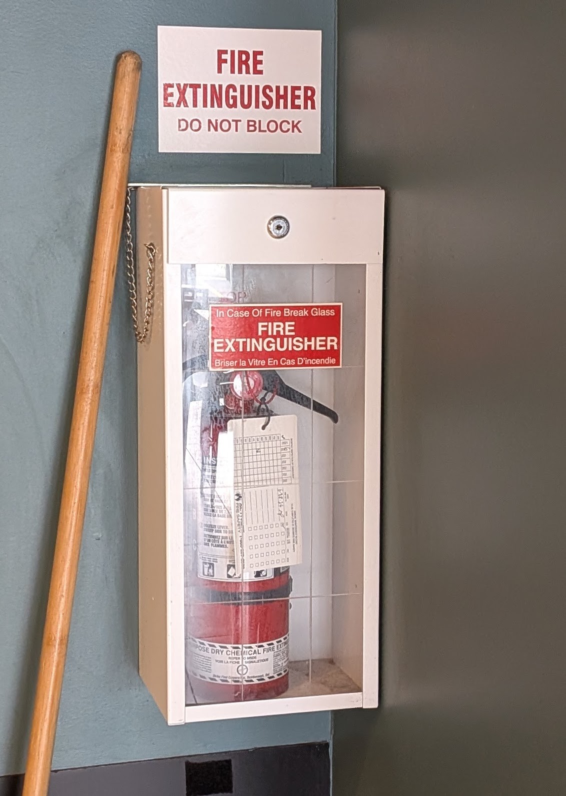 A fire extinguisher, in a locked cabinet in a cafe. The cabinet door is made of glass. The cabinet is locked.